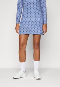 Long-sleeve dress in blue with a geometric pattern, made of stretch fabric. Paired with white athletic socks and shoes.