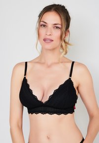 Czarny koronkowy bralet z głębokim dekoltem w kształcie litery V, z falbaniastymi brzegami, regulowanymi ramiączkami i teksturowanymi wzorami. Prosta, nieusztywniana konstrukcja.