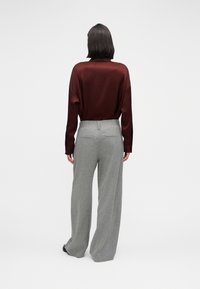 Blouse bordeaux à manches longues associée à un pantalon gris taille haute à jambes larges. La blouse présente une coupe décontractée ; le pantalon a une finition texturée.