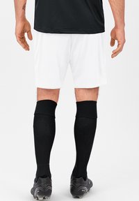 Weiße Sportshorts, schwarze knielange Socken und schwarze Fußballschuhe. Die Shorts haben einen lockeren Schnitt; die Socken weisen ein strukturiertes Webmuster auf.