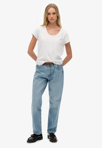 Hvid kortærmet t-shirt, lysblå lige ben jeans, vævet brun bælte, sorte sko med detaljer. Enkel, afslappet påklædning.