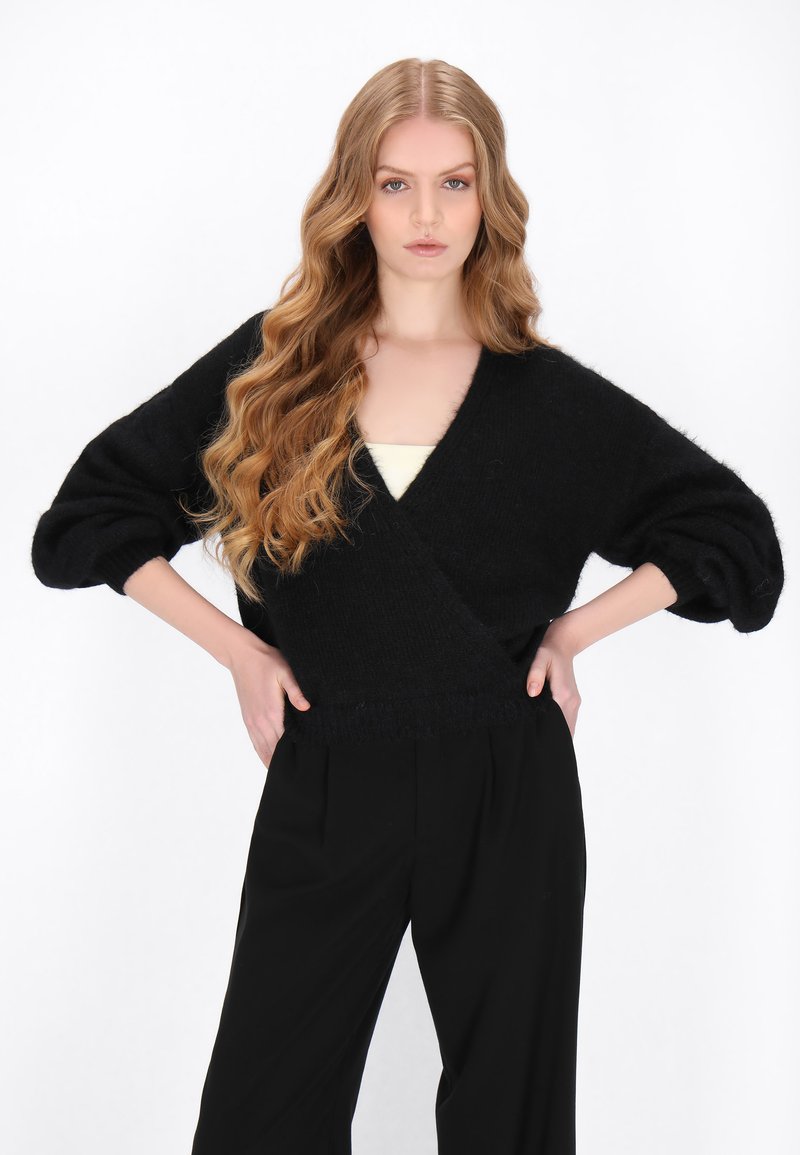Czarny, oversize dzianinowy sweter z głębokim dekoltem w serek i luźnymi rękawami, w zestawieniu z czarnymi spodniami o wysokim stanie. Miękka struktura i swobodny fason.
