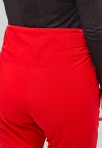 Pantalons taille haute rouges avec une texture lisse et une ceinture élégante. L'arrière présente des coutures sur mesure et un design minimaliste.