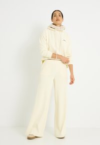 Sudadera color crema y pantalones de pierna ancha, ambos en tela suave. La sudadera cuenta con cordón ajustable y detalles acanalados.