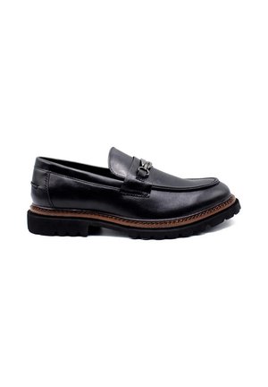 Mocassins en cuir noir avec un bout rond, présentant un accent métallique décoratif. Semelle en caoutchouc épais avec un motif texturé et des coutures contrastées.