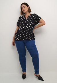 Blusa blu navy con pois bianchi, maniche corte e scollatura a V. Abbinata a jeans skinny blu e tacchi a punta neri. Tessuto di trama liscia.
