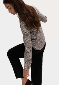 Blusa de manga larga en beige con un diseño de estampado de leopardo en negro y marrón, combinada con pantalones negros. La tela es suave y se ajusta perfectamente.