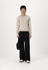 Beige gebreide trui, losse zwarte broek, witte sneakers en een kleine zwarte crossbody tas. Eenvoudig, casual ontwerp met een gestructureerde trui.