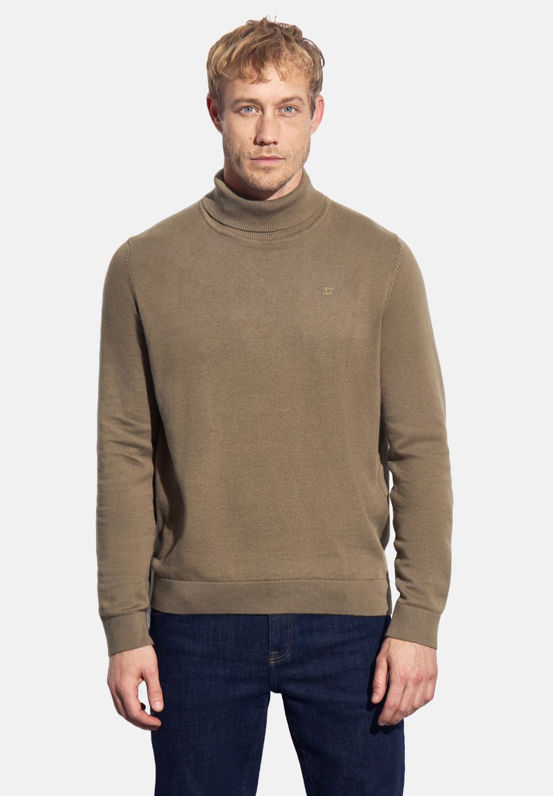Maglione a collo alto marrone realizzato in morbido tessuto a maglia. Presenta un colletto e dei polsini a costine, e un sottile logo sul petto. Abbinato a jeans blu.