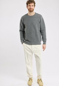 Pull en maille texturée gris avec des poignets et un ourlet côtelés, assorti à un pantalon en velours côtelé écru et des chaussures beige. Design simple et décontracté.