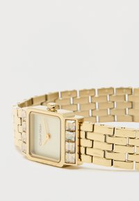 Montre-bracelet en or avec un cadran rectangulaire, un fond vert clair, une aiguille des heures dorée et des accents en cristal sur un côté de la lunette. Bracelet en maillons métalliques.