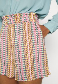 Shorts a fantasia con vita arricciata, design zigzag multicolore in rosa, blu, giallo e marrone. Include tasche laterali.