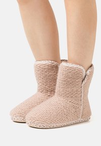 Pink knitted slippers with a textured finish, low ankle height, and decorative white trim along the opening and sole edges.