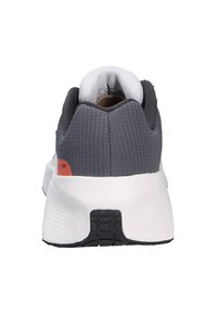 Zapatilla deportiva gris con parte superior de malla texturizada, entresuela blanca y suela de goma negra. Presenta un acento trasero en rojo.