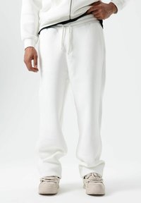 Pantalon de jogging blanc en tissu doux avec une coupe décontractée, doté d'une taille élastique et d'un cordon de serrage, assorti à des baskets légères.