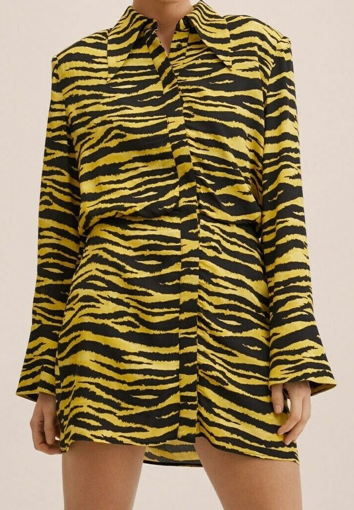 Femme portant une robe-chemise à manches longues à rayures tigre jaune et noir, avec un col et des boutons sur le devant, mains détendues le long du corps.