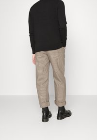 Pull noir, pantalon à motif pied-de-poule avec deux poches arrière, retroussé aux chevilles, assorti à des bottines noires.