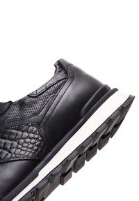 Basket noire avec un mélange de cuir lisse et texturé, présentant un motif tissé, une semelle blanche et un design de semelle durable pour une meilleure adhérence.