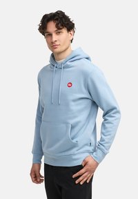 Sudadera ligera azul clara hecha de una mezcla de algodón, con un bolsillo canguro frontal, cordones y un pequeño logo rojo en el pecho.