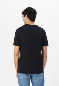Camiseta negra de mangas cortas con un sencillo cuello redondo, hecha de algodón, mostrada por la parte de atrás, combinada con jeans de mezclilla azul claro.