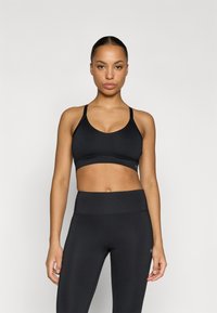 Čierna športová podprsenka s tenkými nastaviteľnými ramienkami a širokým pásom pod prsiami, kombinovaná s vysokým pásom čiernych legín. Hladká textúra a priliehavý dizajn.