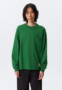 Green long-sleeve t-shirt made of cotton, featuring a front pocket, ribbed neckline, and a tag at the hem. Smooth texture.