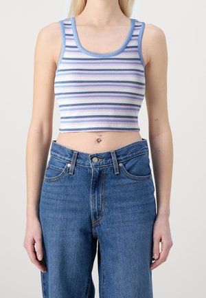 Junge Person, die ein gestreiftes Crop-Top in Blau, Weiß, Pink und Lila trägt, kombiniert mit hoch taillierten blauen Jeans und einem Bauchnabelpiercing.
