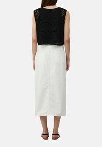 Zwarte gehaakte crop top met hexagonale patronen, gecombineerd met een middellange, witte denimrok met achterzakken. Bruine sandaalband details zichtbaar.