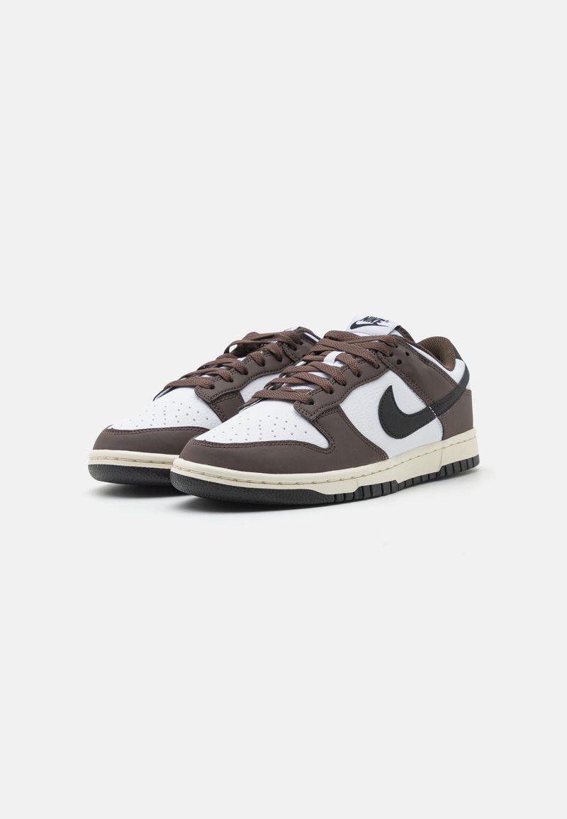 Baskets Nike avec un dessus en cuir blanc, des accents en cuir marron et un swoosh noir. Comprend des perforations sur la partie avant et une semelle en caoutchouc texturée.