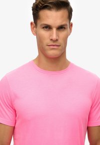 Camiseta rosa de cuello redondo en suave tela de algodón, mangas cortas, diseño ajustado, textura lisa y sin patrones ni acentos visibles.