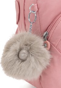 Zaino rosa con portachiavi in peluche beige a pom-pom, dotato di hardware metallico e tessuto texturizzato. Dettaglio della cerniera e tasca laterale visibili.