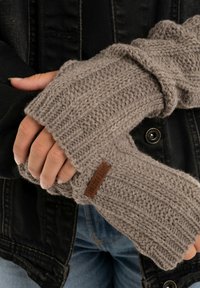 Gebreide vingerloze handschoenen in lichtgrijs, met een geribbelde textuur en een leren label. Het materiaal is zacht en warm, waardoor vingermobiliteit mogelijk is.