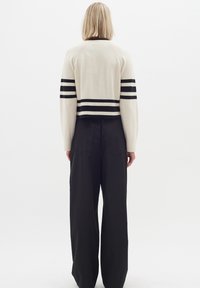 Krämfärgad kortärmad tröja med svarta horisontella ränder på ärmarna, ribbad textur, i kombination med svarta löst sittande byxor.