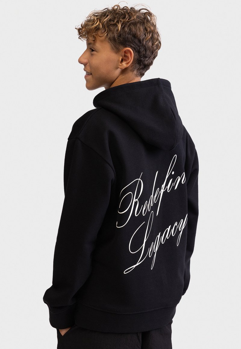 Juodas gobtuvas, pagamintas iš minkštos medžiagos, su dideliu baltu užrašų tekstu ant nugaros, sakant „Redefin Legacy“. Standartinio kirpimo, turintis kišenę kanguru.