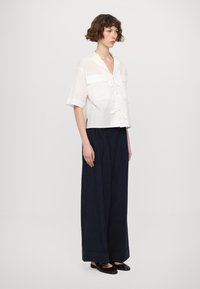 Witte cropped shirt met korte mouwen, een strik aan de voorkant en twee opgestikte zakken, gecombineerd met hoge taille marineblauwe wijde broek. Geweven stof.