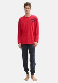 Chemise rouge à manches longues avec un texte marine "LA RÉALITÉ EST CRÉÉE PAR L'ESPRIT", assortie à un pantalon bleu marine foncé, en tissu doux, coupe décontractée.
