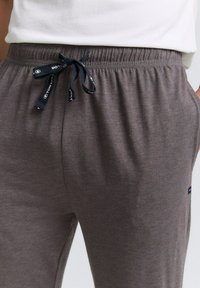 Joggers en coton gris avec une taille élastique à cordon, présentant une texture lisse et des poches latérales. Étiquette de marque cousue sur le côté inférieur.