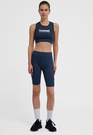 Granatowy sportowy top crop i dopasowane spodenki rowerowe, z logo na piersi, wykonane z elastycznej tkaniny o gładkiej strukturze. Czarne buty sportowe i białe skarpetki.