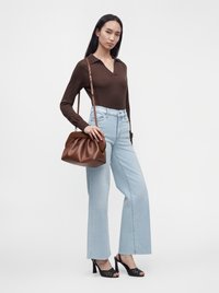Jeune femme portant un haut marron à manches longues, un jean large bleu clair, des sandales noires à talons, portant un sac en cuir marron à l'épaule.