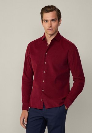 Bordeaux langekoor shirt met een button-down kraag, met een gladde textuur en een subtiele glans, gecombineerd met donkerblauwe broeken.