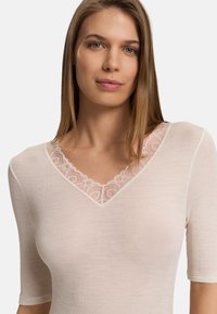 Jasnobeżowa koszulka z ribbed teksturą, dekoltem w kształcie V, ozdobiona różową koronką w kwiatowy wzór, z krótkimi rękawami.