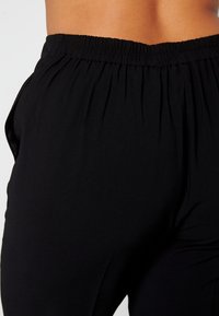 Zwarte, lichte broeken met een elastische tailleband, voorzien van geraffineerde stofdetails en een gladde textuur. Het ontwerp omvat zijzakken.