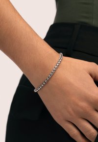 Pulsera de cadena plateada, eslabones redondos, acabado pulido, llevada en la muñeca, combinada con un atuendo oscuro, textura sutil con diseño entrelazado.