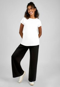 Maglietta bianca a maniche corte abbinata a pantaloni neri larghi e sneakers bianche. Il tessuto sembra morbido; i pantaloni hanno un design a gamba larga.