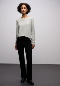 Světlé šedé tričko s dlouhým rukávem a volným střihem, doplněné černými kalhotami s rovnými nohavicemi. Hladká látka a jednoduchý design bez ozdob.