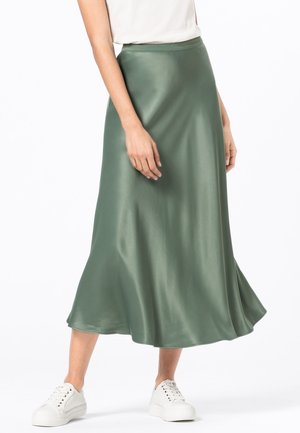 Satin grøn midi-nederdel med en glat tekstur og en A-formet silhuet, med en tætsiddende talje og flydende kant. Båret med hvide sneakers.