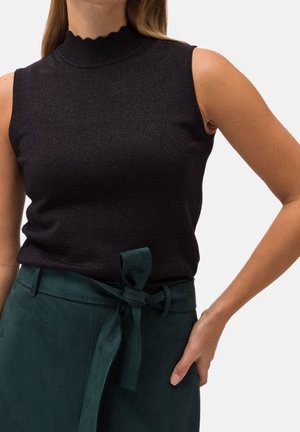 Haut noir sans manches avec col montant, associé à une jupe taille haute vert foncé, ornée d'une ceinture en tissu nouée en un nœud à la taille.