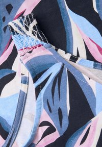 Květinový vzorovaný textil v modré, růžové a černé barvě s designem na závodní záda. Má hladký povrch a šité okraje. Detailní pohled.