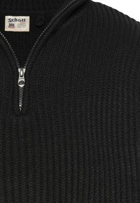 Pullover nero in maglia con texture a coste, caratterizzato da un collo con mezza cerniera e un'etichetta con la scritta "Schott" nella zona interna del colletto.