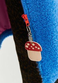Červený ťahák na zips v tvare huby pripevnený na modrom flísovom oblečení s pozadím z leopardieho vzoru.
